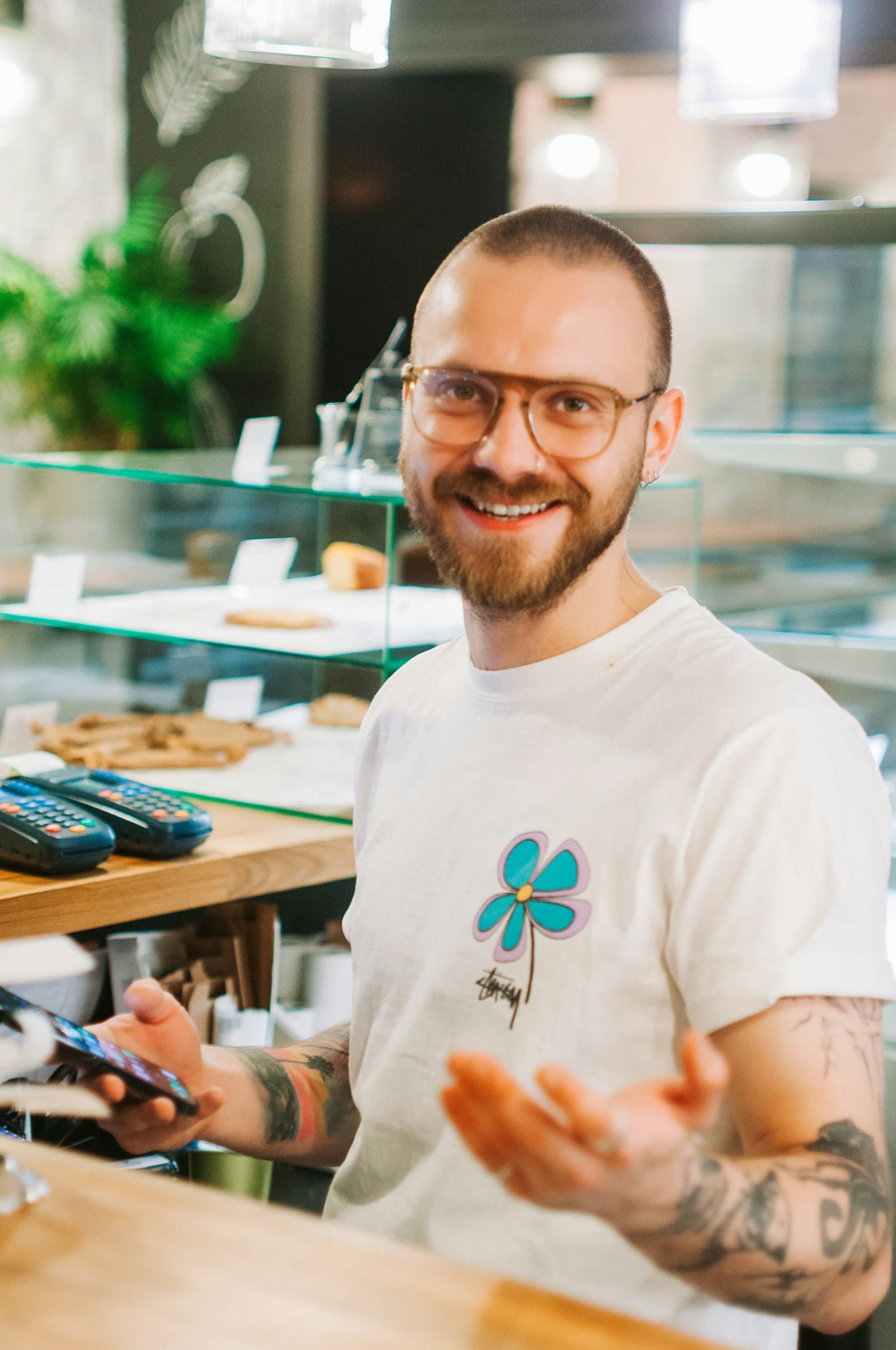 Empreendedor sorrindo com o celular na mão, no balcão do próprio negócio