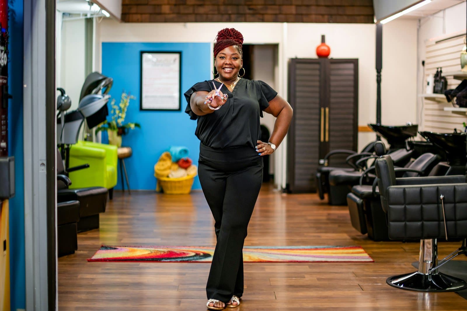 Cabeleireira sorrindo e confiante no próprio salão, organizado e colorido